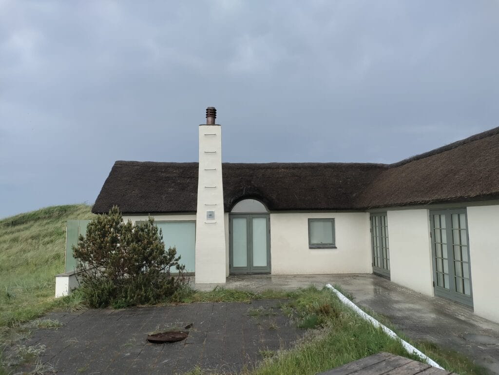 Hvidt stråtækt hus ved klitterne på en overskyet dag