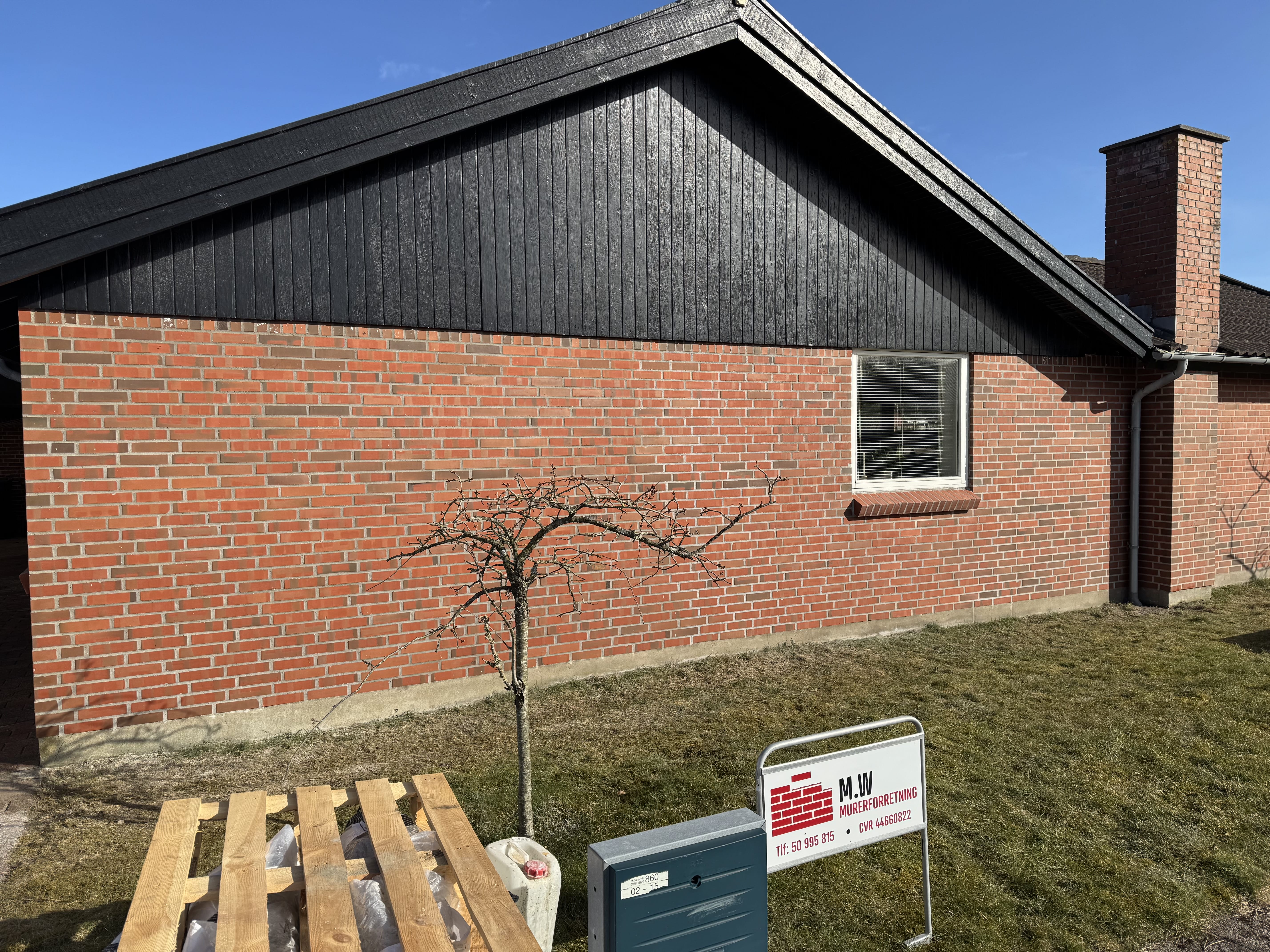 Rødt murstenshus med sort træbeklædning og græsplæne