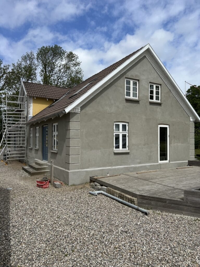 Hus under renovering med gråt puds og stillads